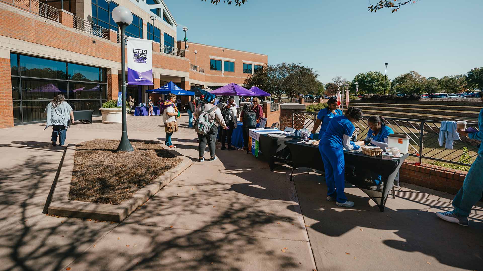 Wide shot of tables set up outside the MGA Student Life Center. Students can be seen receiving information from different booths.